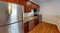 This single-story space in Winston-Salem, NC is designed with a consistent, cohesive aesthetic throughout. Rich, warm-toned hardwood-style flooring flows seamlessly across the living areas and bedrooms, creating a unified and inviting atmosphere. The living area is open and airy, receiving natural light through a front-facing window, and is equipped with a ceiling fan for added comfort.

The kitchen is a standout feature, showcasing rich cherry-toned cabinetry that extends to the upper walls for generous storage. Granite countertops run along the workspace, complemented by a full suite of stainless steel appliances, including a refrigerator, electric range, built-in microwave, and dishwasher. A peninsula with a shiplap-style base and matching granite top connects the kitchen to the living space, offering additional seating or workspace.

The bedrooms continue the hardwood-style flooring and neutral wall tones, each fitted with ceiling fans and windows that allow natural light. The bathroom features light tile flooring, a granite-topped vanity with matching cabinetry, and a clean, functional layout. Throughout, the space maintains a neutral color palette and clean finishes that create a bright, well-maintained environment.