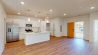 This single-floor residence presents a clean, modern design characterized by an open-concept layout and a bright, neutral color palette. The kitchen serves as the centerpiece of the main living area, featuring white shaker cabinetry extending to the ceiling, a classic subway tile backsplash, stainless steel appliances including a refrigerator with ice maker, electric range, and built-in microwave. A large central island with a built-in sink and white countertops provides both additional workspace and a natural gathering point, illuminated by stylish pendant lighting. The open living area extends seamlessly from the kitchen, with light wood-tone flooring throughout the common spaces creating a cohesive and airy feel.

The bedrooms are carpeted and include ceiling fans, with at least one bedroom offering direct outdoor access through sliding glass doors that bring in generous natural light and views of a grassy outdoor area. A dedicated laundry room houses full-size top-load washer and dryer units alongside overhead wire shelving. The bathroom features a white vanity with drawers, a large mirror, and a tub-shower combination. A spacious walk-in closet with multiple hanging rods and a built-in vanity adds practical storage. The overall ambiance is fresh, functional, and move-in ready.