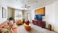 Located in Queen Creek, Arizona, this well-appointed one-bedroom, two-bathroom residence offers a thoughtfully designed single-floor layout. The living room is a welcoming, generously sized space featuring plush carpet, crown molding, a ceiling fan, and large windows that invite natural light. A glass door provides direct access to a private balcony, extending the living area outdoors.

The kitchen is a functional highlight, boasting rich warm-toned cabinetry, granite countertops, a kitchen island with a double sink, track lighting, and black appliances including a refrigerator, range, and built-in microwave. Wood-look flooring grounds the space with a clean, durable finish.

The bedroom is a comfortable retreat with plush carpet, a ceiling fan, and wide windows dressed with sheer curtains and blinds. A dedicated closet provides ample storage.

Both bathrooms are well-appointed, featuring warm wood-toned cabinetry, granite-style countertops, and tub-shower combinations with tiled surrounds. One bathroom showcases wood-look flooring and a large vanity mirror, adding a refined touch.

A hallway connects the rooms efficiently, contributing to the home's cohesive and functional flow throughout.