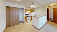 Located at 1302 Hemmingway Dr. in Fairborn, Ohio, this single-floor unit offers a practical and comfortable layout designed for everyday living. The kitchen is well-equipped with warm honey-toned wood cabinetry, white appliances including an electric range and refrigerator, a double stainless steel sink, and light tile flooring. A peninsula counter provides additional workspace and opens toward the adjacent living area, which features neutral carpeting and a sliding wood-panel door leading to a built-in shelving closet for added storage. The living area is bathed in natural light through a large picture window that frames outdoor views, and features vaulted ceiling details that lend a sense of openness to the space. The bedroom is a well-proportioned, carpeted room with clean white walls, warm wood baseboards, and a sliding mirrored closet. The full bathroom is finished with light tile flooring, a single-sink oak vanity with a framed mirror, and a tub-shower combination. A stacked washer and dryer unit is conveniently integrated into the bathroom area, providing in-unit laundry. Throughout the unit, consistent warm wood trim and neutral tones create a cohesive and understated aesthetic.