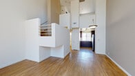 Located at 21021 Vanowen St in Canoga Park, California, this two-story residence offers a thoughtfully designed layout with a striking blend of open, airy spaces and functional living areas. The main level immediately impresses with its dramatic double-height ceilings in the living area, flooding the space with natural light through floor-to-ceiling windows fitted with vertical blinds. A sleek black fireplace anchors the living room, complementing the warm wood-style flooring that extends throughout the lower level. An open-plan layout connects the living area to the kitchen, which is outfitted with rich dark cabinetry, light countertops, stainless steel appliances including a full-size refrigerator, and a window above the sink for added brightness. A carpeted staircase with a white handrail and open railing detail leads to the upper level, where the bedrooms are finished with plush carpet. One bedroom features mirrored sliding closet doors, while another offers a unique architectural niche detail. The bathroom is clean and modern, featuring a wood-toned vanity with a white countertop, a large wall mirror, and a glass-enclosed shower-tub combination with a high window for natural light.