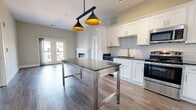 This contemporary apartment offers a harmonious blend of style and functionality. The open-concept layout creates a seamless flow between the living spaces, enhancing the sense of spaciousness. The kitchen is a highlight, boasting pristine white cabinetry, stainless steel appliances, and a stylish subway tile backsplash. Pendant lighting adds a touch of industrial chic.

The living area is anchored by a modern electric fireplace, providing both warmth and ambiance. French doors lead to a private balcony, allowing natural light to flood the space and offering views of the surrounding area. Wood-look flooring runs throughout, complementing the neutral color palette of whites and soft beiges.

The bathroom features a large walk-in shower with marble-look tiling and a glass enclosure, creating a spa-like atmosphere. Bedrooms are generously sized with plush carpeting and ample natural light from large windows. 

Additional amenities include a ceiling fan for comfort, and the apartment's single-floor layout ensures easy accessibility. This thoughtfully designed space combines modern aesthetics with practical living, perfect for those seeking a contemporary urban lifestyle.