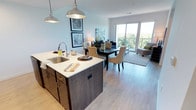 Located at 2202 S Kinnickinnic Ave in Milwaukee's Bay View neighborhood, this single-floor residence offers a thoughtfully designed open-concept layout that seamlessly connects the kitchen, dining, and living areas. The galley-style kitchen is outfitted with dark espresso cabinetry, white quartz countertops, stainless steel appliances including a range, microwave, and refrigerator, and a central island with a built-in sink illuminated by industrial-style pendant lighting. Light hardwood flooring flows throughout the main living areas, adding warmth and continuity. The dining area transitions naturally into a comfortable living room bathed in natural light, anchored by large floor-to-ceiling windows and a sliding glass door that opens to a private balcony with sweeping treetop views. The bedroom is a serene retreat featuring plush carpeting, generous closet space, and expansive windows that frame lush outdoor greenery. A second bedroom also enjoys large windows with scenic views and vaulted ceiling lines. The full bathroom is clean and contemporary, featuring a wide vanity with under-mount sink, dark cabinetry, a large mirror, and a shower-tub combination. Throughout the residence, neutral tones and clean architectural lines create a bright, modern ambiance well-suited to urban living.