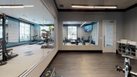 Located at 5500 Home Valley Dr in Raleigh, NC, this well-appointed fitness center offers a comprehensive workout environment designed for both functionality and aesthetic appeal. The space is spread across a single floor and is divided into distinct zones that cater to a variety of exercise needs.

The main workout area features a bold, contemporary design highlighted by teal accent walls, neutral tones, and a striking checkered tile floor. Overhead, linear pendant lighting and a ceiling fan ensure the space is well-lit and comfortable. Large windows with horizontal blinds line the walls, allowing ample natural light to fill the room while providing views of the surrounding exterior.

Cardio equipment, including treadmills and elliptical machines, is thoughtfully arranged in a dedicated section near the windows, offering natural light during workouts. The strength training zone houses a power rack, adjustable bench, dumbbells, kettlebells, medicine balls, and a multi-functional cable machine, providing a thorough free-weight and resistance training experience.

A separate studio room, enclosed with floor-to-ceiling glass walls and a large pass-through window, opens visually to the main floor. This room features hardwood-style flooring, wall-mounted TVs, and stationary bikes, making it ideal for cycling classes or focused training sessions. Wall-mounted TVs throughout the facility enhance the overall workout experience.