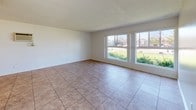 Located at 11414 215th St in Lakewood, California, this single-story residence offers a clean, functional layout with consistent finishes throughout. The living area is generously sized, featuring warm-toned tile flooring, a ceiling fan with light fixture, and a textured ceiling. Large front-facing windows flood the space with natural light and provide views of the surrounding neighborhood's greenery, creating an open and airy atmosphere.

The kitchen is efficiently arranged in a U-shaped configuration, offering ample white cabinetry for storage, granite-style countertops, a double-basin sink, and white appliances including an electric range. The tile flooring continues seamlessly from the living area into the kitchen, reinforcing a cohesive design.

The bedrooms are carpeted for comfort and each include windows with vertical blinds that allow for natural light and privacy. Ceiling fans are present to support ventilation and comfort. Closet space is also provided in the bedrooms.

The bathrooms are well-appointed with granite-topped white vanities, large mirrors, and tile flooring. One bathroom features a full tub and shower combination with built-in shelving, while another includes a dedicated vanity area. Both spaces maintain a clean, neutral aesthetic throughout.