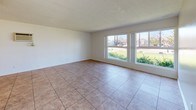 Located at 11414 215th St in Lakewood, California, this single-story residence offers a clean, functional layout with consistent finishes throughout. The living area is generously sized, featuring warm-toned tile flooring, a ceiling fan with light fixture, and a textured ceiling. Large front-facing windows flood the space with natural light and provide views of the surrounding neighborhood's greenery, creating an open and airy atmosphere.

The kitchen is efficiently arranged in a U-shaped configuration, offering ample white cabinetry for storage, granite-style countertops, a double-basin sink, and white appliances including an electric range. The tile flooring continues seamlessly from the living area into the kitchen, reinforcing a cohesive design.

The bedrooms are carpeted for comfort and each include windows with vertical blinds that allow for natural light and privacy. Ceiling fans are present to support ventilation and comfort. Closet space is also provided in the bedrooms.

The bathrooms are well-appointed with granite-topped white vanities, large mirrors, and tile flooring. One bathroom features a full tub and shower combination with built-in shelving, while another includes a dedicated vanity area. Both spaces maintain a clean, neutral aesthetic throughout.