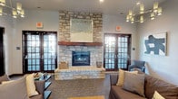 This single-floor residence offers a thoughtfully designed layout that blends comfort and functionality. The entryway welcomes you with rich, dark wood-style flooring and neutral-toned walls, setting a clean and modern tone throughout. A keypad entry system is conveniently positioned near the front door, adding a layer of security.

The open-concept main living area transitions seamlessly from hardwood-style flooring to plush carpeting, delineating the living and dining zones while maintaining a cohesive aesthetic. Crown molding accents the ceilings, adding a refined architectural touch. The kitchen features gleaming granite countertops with pendant lighting overhead, complementing the warm, neutral color palette found throughout the unit. Interior columns provide subtle definition between spaces without compromising the open feel.

Hallways lead to additional rooms, each finished with consistent neutral tones and paneled interior doors for a polished look. Bifold closet doors offer practical storage solutions.

Residents also enjoy access to a shared amenity lounge featuring a dramatic floor-to-ceiling natural stone fireplace with a thick wood mantel as its centerpiece. Flanked by French doors that flood the space with natural light, the lounge is furnished with comfortable seating, creating an inviting communal retreat ideal for relaxation or socializing.