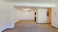 Located at 4563 S Whitnall Ave in St. Francis, Wisconsin, this single-floor unit offers a thoughtfully arranged layout with clearly defined living, sleeping, and functional spaces. The living area is generously proportioned, featuring neutral carpet flooring, crisp white walls, a ceiling fan, and a baseboard heating unit. Structural beam detailing along the ceiling adds subtle architectural character, while an open passage leads directly into the kitchen, promoting a connected flow between spaces.

The galley-style kitchen is well-appointed with dark espresso cabinetry lining both walls, dark granite-style countertops, wood-look flooring, and black appliances including a range with oven and a full-size refrigerator. An overhead exhaust fan and ample upper and lower cabinet storage make this a highly functional cooking space.

The bedrooms are carpeted and feature louvered bi-fold closet doors, white walls, and baseboard heating. One bedroom includes a window with an exterior view, allowing natural light to fill the room. A wall-unit air conditioner is present in one of the rooms for additional climate control.

The bathroom features earthy stone-look tile flooring, tiled tub surround, a toilet, and a dark vanity with granite-style countertop, creating a cohesive and practical finish throughout.