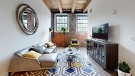 Located at 150 Oakland St in Mansfield, MA, this industrial-chic loft masterfully blends historic character with contemporary design. The single-floor layout is anchored by a dramatic living area showcasing exposed brick walls, soaring wood-beamed ceilings with visible ductwork, and large multi-pane factory-style windows that flood the space with natural light and offer views of the surrounding greenery. Wide-plank hardwood flooring flows throughout the main living area, complementing the warm, textured aesthetic.

The open living room offers generous proportions, with the exposed structural beams adding striking architectural interest overhead. The kitchen is well-appointed with rich dark cabinetry, stone countertops, a full suite of stainless steel appliances including a gas range, microwave, dishwasher, and refrigerator, as well as a classic subway tile backsplash.

The bedroom continues the loft's industrial character with exposed brick, tall ceilings, and large windows, creating a bright and airy retreat. The bathroom features clean, modern finishes with large-format tile flooring, a full tub-and-shower combination, and a dark wood vanity with a stone countertop. A bold, paneled entry door adds a refined touch to the entryway, completing this distinctive and stylish urban loft.