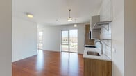 This single-floor residence presents a thoughtfully designed open-concept layout, where the living area and kitchen flow seamlessly together. Rich hardwood flooring runs throughout the unit, providing warmth and continuity across every room. Large sliding glass doors and floor-to-ceiling windows in the living area invite generous natural light and frame views of the surrounding urban streetscape, including a notable arched brick structure across the way.

The kitchen is well-appointed with stainless steel appliances, including a gas range, built-in microwave, refrigerator, and dishwasher. Two-toned cabinetry—combining light upper cabinets with wood-grain lower units—pairs with a white subway tile backsplash and light countertops for a clean, contemporary aesthetic.

The bedrooms are bright and neutral, featuring white walls, hardwood floors, and ample closet space, with one room offering dual sliding-door closets. A wall-mounted split air conditioning unit is present for climate control.

The bathroom stands out with a walk-in glass shower clad in vertical white tile, a bold blue vanity with chrome hardware, a mirrored medicine cabinet, and polished concrete flooring, adding a distinctive design element to the overall space.