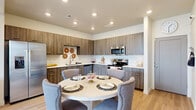 This thoughtfully designed two-story home offers a comfortable and modern living experience across two distinct levels. The main floor features an open-plan kitchen, dining, and living area that serves as the heart of the home. The kitchen is outfitted with sleek wood-grain cabinetry, stainless steel appliances including a refrigerator, microwave, and dishwasher, complemented by clean white countertops and light hardwood-style flooring. A round dining table sits adjacent to the kitchen, creating a seamless flow into the living space, which is brightened by large windows and recessed lighting throughout.

Upstairs, the more expansive second floor houses all three bedrooms, a full bathroom, two closets, and a hallway connecting the spaces. The bedrooms feature plush carpeting and windows that invite natural light, with the generously sized primary bedroom offering ample room for a full furniture arrangement. The closets include built-in shelving for organized storage. The shared bathroom presents a clean, contemporary aesthetic with wood-grain vanity cabinetry, a white quartz countertop, a large mirror, and a shower-tub combination. A staircase connects both floors, completing this practical and stylish layout.