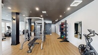 Located at 927 W Morgan St in Raleigh, NC, this well-appointed fitness center offers a comprehensive exercise facility across a single open floor. The space is designed with a modern industrial aesthetic, featuring light hardwood-style flooring that contrasts sharply with the dark-painted ceiling, which showcases exposed ductwork and recessed lighting throughout.

The fitness center is equipped with an extensive array of workout equipment to support diverse training needs. Strength training is well covered with a multi-function cable machine system, a Smith machine with an adjustable bench, a dedicated dumbbell rack with a full set of weights, kettlebell storage, and resistance bands. A Matrix-branded cable station is also present, along with additional weight benches and functional training accessories including medicine balls and stability balls.

For cardiovascular training, the space includes treadmills, elliptical machines, and air resistance bikes. Large wall-mounted mirrors are positioned throughout to allow users to monitor their form during workouts.

Natural light filters in through a bank of large windows along one wall, offering views of an adjacent outdoor pool area and the surrounding Raleigh streetscape. Structural columns with a charcoal finish are integrated into the layout, reinforcing the space's modern industrial character. The overall ambiance is clean, functional, and energizing — a well-rounded facility suited for a full-body fitness regimen.