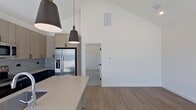 Located at 8940 Drum Dr A in Rowlett, TX, this efficiently designed 480-square-foot, one-bedroom, one-bathroom residence delivers modern style across a single thoughtfully laid-out floor. The kitchen is the standout centerpiece, showcasing soaring vaulted ceilings, light wood cabinetry with matte black hardware, dark lower cabinets, a large quartz-topped island with an undermount sink, subway tile backsplash, and stainless steel appliances including a French door refrigerator, electric range, and over-the-range microwave. Stylish industrial-style pendant lights hang above the island, adding character to the open space. Light wood-look flooring runs throughout the main living and kitchen areas, enhancing the bright, airy atmosphere. The 130-square-foot bedroom features plush carpet, crisp white walls, a ceiling fan with lighting, and a window with outdoor views. It connects directly to a dedicated closet and the full bathroom. The bathroom is finished with matching wood-tone cabinetry, quartz countertops, and wood-look flooring, maintaining design consistency with the rest of the unit. Large windows throughout allow ample natural light, contributing to the home's clean, contemporary ambiance.