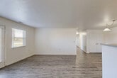 This single-floor unit offers a straightforward and functional layout designed for comfortable everyday living. The open living area is bright and spacious, featuring neutral white walls, a textured ceiling, and wood-look plank flooring that runs consistently throughout the space. A pendant light fixture and a pass-through counter with a raised bar-style divider connect the living area to the kitchen, creating an open and social feel. Natural light enters through a front-facing door with a window and sidelight, enhancing the airy atmosphere.

The kitchen is equipped with warm honey-toned wood cabinetry, light countertops, and white appliances including a refrigerator and range. A window above the laundry area brings in additional natural light and views of the exterior. The bedrooms are well-proportioned with the same consistent wood-look flooring, white walls, and windows fitted with horizontal blinds. The rooms offer ample wall space and closet access, providing practical storage solutions.

The bathroom features a clean, white tub-shower combination with chrome fixtures, maintaining the unit's consistent and understated aesthetic. A hallway connects the main living spaces to the bedrooms and bath, creating an efficient and easy-to-navigate floor plan throughout.