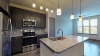 This single-floor residence features a thoughtfully designed open-concept layout, where the living area flows seamlessly into the kitchen. The kitchen serves as a central highlight, showcasing dark espresso cabinetry, granite countertops, and a full suite of stainless steel appliances including a range, microwave, refrigerator, and dishwasher. A large kitchen island with an undermount sink and brushed nickel faucet provides additional workspace and casual seating potential. A mosaic tile backsplash adds a refined decorative touch, while a combination of track lighting and pendant fixtures ensures ample illumination throughout.

Wood-style plank flooring extends through the main living areas, adding warmth and visual continuity. The living space is generously proportioned, receiving natural light through large windows fitted with blinds. Bedroom areas feature ceiling fans and windows with outdoor views, with one bedroom finished in plush carpeting and another with wood-style flooring.

The bathroom is well-appointed with granite countertops, dark cabinetry with chrome hardware, an undermount sink, and a glass-enclosed walk-in shower. Wood-look tile flooring and a large mirror complete the refined, cohesive aesthetic found throughout this well-finished residence.