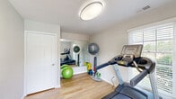Located at The Lofts in Winston-Salem, NC, this dedicated fitness center offers a well-equipped, single-room workout space designed for efficient, functional exercise. The room features light-toned hardwood-style flooring throughout, providing a clean and durable surface ideal for a variety of workouts. Neutral-painted walls and a large wall-mounted mirror enhance the sense of openness, reflecting natural light and making the space feel larger than its footprint suggests. A round flush-mount ceiling light provides consistent overhead illumination to complement the natural light admitted through a slatted window blind. The fitness center is equipped with a treadmill and a rowing machine, along with an array of stability balls, resistance bands, and dumbbells, accommodating both cardiovascular and strength training routines. A ball rack keeps equipment neatly organized. A glazed exterior door provides direct outdoor access and allows additional natural light to fill the room. Fitness center rules are posted on the wall, indicating shared community use. The overall ambiance is clean, bright, and purposeful, making this a practical and welcoming space for residents seeking a convenient on-site exercise option.