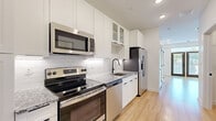 This single-floor residence showcases a thoughtfully designed interior with a clean, modern aesthetic carried consistently throughout. The kitchen is a standout feature, outfitted with white shaker-style cabinetry — including glass-front upper cabinets — and granite countertops that add a touch of elegance. A classic white subway tile backsplash complements the space, while stainless steel appliances, including a range, over-the-range microwave, dishwasher, and French door refrigerator, provide a fully functional cooking environment. Matte black hardware and fixtures lend a refined, contemporary contrast. Light hardwood flooring flows seamlessly throughout the unit, enhancing the bright and airy atmosphere. The living area is generously proportioned, featuring recessed lighting, a ceiling fan, and large French doors that flood the room with natural light and offer views of the surrounding greenery. A bold navy entry door adds a distinctive design accent. The bathroom continues the modern theme with floor-to-ceiling white subway tile, a spacious walk-in shower enclosed by a frameless glass sliding door, and matte black fixtures that echo the hardware found throughout the residence. The overall ambiance is fresh, cohesive, and move-in ready.