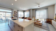 This well-designed single-floor residence offers a thoughtful open-concept layout that seamlessly connects the kitchen, dining, and living areas. The kitchen is a standout feature, showcasing a large quartz-topped island with bar seating, gray cabinetry, a subway tile backsplash, stainless steel appliances, and light wood-look flooring that extends throughout the main living areas. Recessed lighting keeps the space bright and welcoming.

The living area is bathed in natural light through generous windows dressed with horizontal blinds and floor-to-ceiling drape panels, offering outdoor views and a comfortable, airy atmosphere. A ceiling fan adds a practical touch overhead.

The residence includes multiple bedrooms, each featuring plush carpet flooring and large windows that invite natural light. The primary bedroom is distinguished by its spacious feel and tasteful design details, while the secondary bedrooms offer comfortable retreats with ample space.

The bathrooms are finished with quartz countertops, undermount sinks, gray cabinetry, and large-format tile. One bathroom includes a tub-shower combination with full tile surround, while another features a dedicated vanity area with a wide mirror and modern fixtures. Throughout the space, neutral tones and contemporary finishes create a cohesive, modern aesthetic.