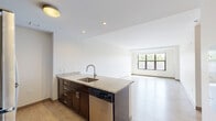 Located at 225 Centre Street in Boston's vibrant Jamaica Plain neighborhood, this well-designed one-bedroom, one-bathroom residence offers a thoughtfully organized layout across a single floor. The open-concept kitchen and living area serves as the heart of the home, where a central kitchen island with granite countertops and an undermount sink creates a natural focal point. Rich dark-cabinetry lines both the island and the galley-style kitchen wall, complemented by a full suite of stainless steel appliances including a refrigerator, electric range, built-in microwave, and dishwasher. Light wood-tone flooring runs throughout, lending warmth and continuity to the space. The living area is bright and open, anchored by a large multi-pane window that invites natural light and offers views of the surrounding Boston streetscape. The generously sized bedroom continues the same light flooring and neutral palette, featuring its own window with city views. The full bathroom is finished with white subway tile surrounding a tub/shower combination, tile flooring, and a vanity with ample storage. A hallway and closet round out the floor plan, providing practical storage solutions within this efficient and modern residence.