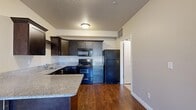 Located at 5332 W Highbury Pkwy in West Valley City, Utah, this one-bedroom, one-bathroom unit offers a thoughtfully designed single-level layout with a functional and efficient use of space throughout.

The kitchen serves as a standout feature, showcasing dark espresso cabinetry, granite countertops, and a full suite of black appliances including an electric range, built-in microwave, dishwasher, and refrigerator. A peninsula with additional counter space adds to the kitchen's utility and creates a natural transition into the living area. Rich hardwood-style flooring runs throughout the kitchen, adding warmth and contrast to the dark cabinetry.

The bedroom is generously sized, finished with plush wall-to-wall carpeting and two windows that allow for natural light and outdoor views. A dedicated walk-in closet provides ample storage with built-in shelving and a full hanging rod.

The bathroom continues the cohesive design aesthetic with matching dark cabinetry, granite countertops, a large vanity mirror with overhead lighting, and clean tile flooring.

A separate laundry room accommodates a full-size washer and dryer side by side, with an overhead shelf for additional storage. Neutral wall tones and consistent finishes throughout create a clean, cohesive ambiance across the entire unit.
