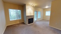 Located at 11400 Olympus Way in Gig Harbor, Washington, this single-floor residence offers a comfortable and functional living environment surrounded by the natural beauty of the Pacific Northwest. The main living area is generously sized, showcasing plush wall-to-wall carpeting that adds warmth underfoot. A tile-surround fireplace serves as a focal point of the room, providing both a visual anchor and a cozy atmosphere during cooler seasons. Track lighting overhead complements the abundant natural light that pours in through multiple large windows fitted with blinds, offering both brightness and privacy. A glass-paneled door leads to an outdoor area, seamlessly connecting the interior to the greenery visible just beyond the windows — a hallmark of the lush Gig Harbor surroundings. The walls are finished in a warm neutral tone, creating a clean and inviting backdrop throughout. The layout is open and airy, lending itself well to a variety of furniture arrangements. The overall ambiance is calm and residential, with thoughtful finishes that balance practicality and comfort in a setting that takes full advantage of its serene, wooded surroundings.