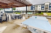 This contemporary apartment complex in Katy, Texas, showcases a striking architectural design with a color palette of deep blue and crisp white. The three-story buildings feature a mix of stone and siding exteriors, creating visual interest and texture. Each unit boasts large windows and private balconies, offering residents ample natural light and outdoor living space.

The property's landscaping is meticulously maintained, with manicured lawns, young trees, and neat pathways surrounding the buildings. A black wrought-iron fence provides security and definition to the grounds. The complex offers an array of outdoor amenities, including a spacious concrete patio area with multiple seating arrangements. A centerpiece of this area is a large fire pit surrounded by comfortable Adirondack chairs, perfect for social gatherings.

Additionally, there's a covered outdoor structure, likely used for community events or as a shared recreational space. The complex also features ample parking and appears to have good accessibility with wide sidewalks throughout. The overall design of the property emphasizes a blend of modern comfort and community-oriented living, making it an attractive option for those seeking a contemporary living experience in a suburban setting.