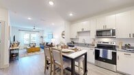 This thoughtfully designed one-bedroom, one-bathroom residence offers an efficient and functional single-story layout that maximizes every square foot. The open-concept living and kitchen area anchors the home, featuring light wood-look flooring and recessed lighting that creates a bright, welcoming atmosphere throughout. The kitchen is outfitted with white shaker cabinetry with matte black hardware, granite countertops, a stainless steel appliance suite including a refrigerator, electric range, microwave, and dishwasher, and a central island with seating — ideal for casual dining and entertaining. The living room is filled with natural light from large windows dressed with sheer curtains, and includes a ceiling fan for added comfort. The bedroom offers plush carpeting, a ceiling fan, a generous window with outdoor views, and access to a dedicated closet. The bathroom features a granite-topped vanity with an undermount sink, wood-tone cabinetry, a large framed mirror, and a shower/tub combination. A practical entryway with built-in storage shelving completes the layout. Clean white walls and consistent finishes throughout lend the space a cohesive, modern aesthetic.