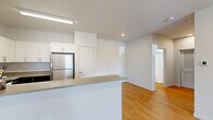Located at 6900 NE 154th Ave in Vancouver, WA, this well-appointed one-bedroom, one-bathroom apartment offers a thoughtfully designed single-floor layout. The open-concept living and kitchen area is anchored by warm light wood flooring that extends throughout the main living spaces, creating a bright and cohesive feel. The kitchen is outfitted with stainless steel appliances — including a refrigerator, range, microwave, and dishwasher — complemented by two-tone cabinetry featuring white upper cabinets and dark lower cabinets, plus a peninsula counter ideal for casual dining or prep work. The spacious living area receives natural light through a large window with outdoor views, and features a wall-mounted HVAC unit for climate control. A private exterior door provides convenient direct access. The bedroom is carpeted for comfort, benefits from natural light via a window with outdoor views, and includes a wide sliding-door closet for ample storage. The bathroom is well-equipped with a full tub and shower combination featuring a curved curtain rod, grab bars for accessibility, and wood-toned flooring. Clean white walls and recessed lighting throughout give the entire unit a modern, move-in-ready appearance.