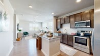 This single-story residence at Allora New Forest in Houston, Texas, offers a thoughtfully designed open-concept layout that seamlessly connects the kitchen, dining, and living areas. The kitchen is a standout feature, showcasing rich dark-brown cabinetry, a classic white subway tile backsplash, granite countertops, and a full suite of stainless steel appliances, including a refrigerator with ice maker, range, microwave, and dishwasher. A central island with granite countertops and bar seating provides additional workspace and a casual dining option.

The living area is bright and welcoming, benefiting from multiple windows fitted with horizontal blinds that invite generous natural light and outdoor views of the surrounding neighborhood. Light wood-tone flooring runs consistently throughout the space, enhancing the open and airy feel, while ceiling fans provide added comfort.

The bedroom is a calm, neutral retreat with its own window and ceiling fan. The full bathroom features subway tile surrounding the soaking tub and shower, a granite-topped vanity with dark cabinetry, and wood-tone flooring. A dedicated laundry area with a full-size washer and dryer adds everyday convenience, complemented by wire shelving for storage.