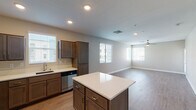 This single-floor residence is designed with an open-concept layout that seamlessly connects the kitchen and living areas, creating a spacious and functional flow throughout the unit. The kitchen is well-appointed with medium-toned cabinetry, light quartz countertops, and a full suite of stainless steel appliances, including a gas range, built-in microwave, refrigerator, and dishwasher. A central island provides additional counter space and serves as a natural dividing point between the kitchen and the expansive living area. Wood-look hard-surface flooring runs throughout the main living spaces, offering a clean and cohesive aesthetic, while recessed lighting and a ceiling fan with light fixture ensure both function and comfort. Multiple windows fitted with horizontal blinds allow natural light to fill the space. The bedroom features plush carpeting, a ceiling fan, and a window with outdoor views. The bathroom is equipped with a full tub and shower combination accented by white tile surround, chrome fixtures, and matching hard-surface flooring, maintaining consistency with the overall neutral and contemporary design palette found throughout the unit.