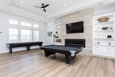 Located at 5073 W Jay Bend Ln in Herriman, Utah, this well-appointed single-floor space offers a generous, open layout filled with natural light and modern finishes throughout. The interior is anchored by wide-plank light hardwood flooring that flows seamlessly across the entire floor plan, creating a warm and cohesive aesthetic.

The kitchen is a standout feature, showcasing white shaker-style cabinetry extending to the ceiling, granite countertops with subtle veining, and a mosaic tile backsplash in neutral tones. A central island with seating provides a functional gathering point, while stainless steel appliances — including a French door refrigerator and dishwasher — complete the well-equipped space. High ceilings amplify the sense of openness.

The expansive recreation and lounge area is equally impressive, featuring a coffered ceiling with recessed lighting and dual ceiling fans. A floor-to-ceiling tile-clad fireplace with a linear insert serves as a dramatic focal point, flanked by built-in shelving. Large windows and glass double doors flood the room with natural light and offer views of the surrounding neighborhood. The space comfortably accommodates a pool table and shuffleboard, making it ideal for entertainment. Two hallways provide convenient connectivity throughout the layout, ensuring smooth flow between areas.
