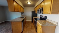 This upgraded three-floor townhome in Ann Arbor, Michigan offers a well-appointed layout with three bedrooms and two and a half bathrooms. The kitchen is a standout feature, designed in a galley-style configuration with warm honey-toned cabinetry, granite countertops, and a full suite of stainless steel appliances including a refrigerator, electric range with microwave above, and dishwasher. Rich hardwood-style flooring runs throughout the kitchen and main living areas, lending warmth and continuity to the space. A peninsula with a built-in sink adds both functionality and an open sightline toward the adjacent living area. The bedrooms are generously sized, finished with plush carpeting and neutral-toned walls accented by clean white crown molding, creating a calm and comfortable atmosphere. Natural light filters in through windows in the main bedroom, enhancing the airy feel. The bathrooms are finished with tile flooring that complements the granite vanity tops and warm wood cabinetry, with one full bath featuring a glass-enclosed walk-in shower with tile surround. The lower level includes a carpeted utility or storage area. Throughout, the home reflects thoughtful upgrades and a cohesive, move-in-ready aesthetic.