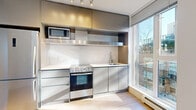 This thoughtfully designed two-bedroom, two-bathroom residence offers a clean, contemporary aesthetic throughout its efficiently organized single-floor layout. Light-toned wood-style flooring runs continuously through the living areas and bedrooms, creating a cohesive, modern feel.

The kitchen is a standout feature, outfitted with sleek stainless steel appliances including a full-size refrigerator, oven with range, built-in microwave, and a stainless steel range hood. Flat-panel cabinetry in a muted metallic finish extends to the ceiling for generous storage, complemented by white countertops and a large floor-to-ceiling window that floods the space with natural light and provides views of the surrounding urban landscape.

The bedrooms are bright and airy, with crisp white walls and large windows that allow sunlight to cast across the light flooring. Both bathrooms are finished with neutral tile flooring, white soaker tub-shower combinations, modern floating vanities with white countertops, and large mirrors with chrome fixtures throughout.

The unit also includes a dedicated laundry area, a closet, and multiple hallways for practical circulation. A spacious outdoor balcony with glass railings offers open views of the neighboring cityscape under wide, clear skies — an ideal spot for enjoying the outdoors. The overall ambiance is clean, minimalist, and move-in ready.