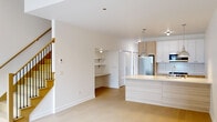 This contemporary two-floor space showcases a clean, modern aesthetic defined by crisp white walls, light hardwood flooring on the upper level, and polished concrete floors on the lower level. The open-concept main living area flows seamlessly into a well-appointed kitchen featuring a large island with a white quartz countertop, a stainless steel refrigerator, gas range, microwave, and a combination of white upper cabinets and light wood lower cabinetry. Industrial-style pendant lights hang above the island, adding a stylish focal point. A built-in desk with open shelving is tucked into the living area, offering a convenient workspace. A sliding barn door with stainless steel hardware provides access to a utility area housing the electrical panel. The lower level also includes a bathroom with a walk-in glass shower, modern vanity, and polished concrete flooring. Upstairs, the bedrooms are bright and airy, with large black-framed windows offering outdoor views of surrounding greenery. One bedroom features direct access to a private balcony. A spacious walk-in closet with built-in shelving and hanging rods offers generous storage. An additional full bathroom upstairs includes a clean white vanity and tiled shower. A wall-mounted mini-split system provides climate control. Throughout, the space maintains a minimalist, move-in-ready character.