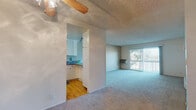 This single-floor unit is thoughtfully laid out to maximize functionality across its living spaces. The living area is generously sized, featuring soft wall-to-wall carpeting, a ceiling fan with a light fixture, and a textured ceiling. A sliding glass door opens to a private balcony, allowing natural light to fill the room while offering pleasant outdoor views of surrounding greenery. A wall-mounted air conditioning unit provides climate control directly in this space.

The kitchen is accessed through an open passageway and features a galley-style layout with warm hardwood flooring, white cabinetry, dark granite-style countertops, a built-in electric range, a full-size refrigerator, and a dishwasher. Track lighting overhead brightens the workspace efficiently. A pass-through counter connects the kitchen visually to the main living area.

The bedroom is a well-proportioned, carpeted room with a large window that brings in ample natural light and offers views of the surrounding neighborhood. A baseboard heater runs along one wall, ensuring comfortable temperatures year-round.

The bathroom is clean and bright, featuring a full tub and shower combination with white subway tile surround, built-in shelving niches, and classic fixtures. The overall ambiance of the unit is light, neutral, and move-in ready.