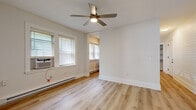 Located at 1416 Lewis Drive in Lakewood, Ohio, this single-floor 2-bedroom, 1-bathroom residence offers a clean, modern aesthetic with thoughtful finishes throughout. Light-toned hardwood flooring runs continuously across all rooms, creating a cohesive and airy feel. The spacious primary bedroom is notably generous in size, featuring multiple windows with slatted blinds that invite abundant natural light, a ceiling fan with integrated lighting, and baseboard heating for year-round comfort. The second bedroom mirrors the same bright, minimalist design with its own windows and baseboard heater. The kitchen is a functional galley-style space outfitted with warm wood-grain upper and lower cabinetry, white quartz countertops, a deep stainless steel sink with a modern spring-neck faucet, and stainless steel appliances including a range with overhead ventilation. A connecting hallway with light gray LVP flooring links the rooms efficiently, with an electrical panel visible along the wall. The bathroom features contemporary cabinetry with matching wood-grain finishes and white countertops, consistent with the kitchen design. Clean white walls and crisp white trim throughout the space reinforce a fresh, move-in-ready presentation.