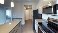 This well-appointed 2-bedroom, 2-bathroom residence is thoughtfully designed with a contemporary aesthetic and functional layout spread across a single floor. Dark hardwood-style flooring runs throughout, providing a cohesive and polished look that complements the neutral gray and taupe color palette found in every room.

The kitchen serves as a central hub of the home, featuring stainless steel appliances including a refrigerator, range, microwave, and dishwasher. Light wood cabinetry with modern hardware pairs with a quartz-style countertop, while a center island with pendant lighting overhead offers bar-style seating — ideal for casual dining or entertaining. The kitchen flows naturally toward the entryway and living areas.

The bedrooms are bright and open, benefiting from windows that invite natural light and provide views of the surrounding area. The clean, minimalist walls and dark flooring create a calm and versatile space.

Both bathrooms mirror each other in style, each featuring a single-sink vanity with contemporary cabinetry, a large mirror, a glass-enclosed walk-in shower, and built-in open shelving for storage. Dark hardwood-style flooring continues into these spaces, tying the design together seamlessly.

Overall, the residence delivers a clean, modern living experience with quality finishes and a practical, well-organized floor plan.