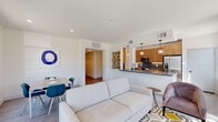 This single-floor residence showcases a thoughtfully designed open-concept layout that seamlessly connects the living, dining, and kitchen areas. The living room is bright and airy, featuring large sliding glass doors and multiple windows that invite abundant natural light and provide views of the surrounding landscape. A ceiling fan adds both function and style to the space, which is finished with warm wood-look flooring.

The kitchen is a standout feature, outfitted with flat-front wood-tone cabinetry, stainless steel countertops, a gas range, built-in microwave, and a full-size stainless steel refrigerator. A dark-topped breakfast bar separates the kitchen from the living area, while pendant lighting adds a modern touch overhead. A tile backsplash and a window overlooking the outdoors complete the space.

The bedrooms are carpeted and well-lit, each offering outdoor views through sliding or standard windows. One bedroom includes a dedicated walk-in closet. The bathroom features a wood-tone vanity with a gray countertop, an LED-lit mirror, and a tub-shower combination. In-unit laundry is neatly tucked into a dedicated closet, rounding out the practical and polished design of this residence.