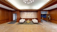 Located at 8 W King St in the heart of Lancaster, PA, The Intel lobby is a sophisticated and generously proportioned commercial space that makes a strong first impression. The entrance features a glass-enclosed vestibule with brass-trimmed automatic doors set against warm travertine marble flooring that extends throughout the main lobby area, lending the space a timeless, upscale character.

The interior design blends classic and contemporary elements seamlessly. Rich, dark wood paneling lines the walls, accented by crown molding and recessed coffered ceilings that add architectural depth. A statement chandelier with globe-shaped lights serves as a focal centerpiece, casting warm, ambient light across the space.

The lobby is divided into distinct functional zones. A central lounge area features crisp white upholstered seating arranged around a gold-toned glass coffee table, positioned beneath the boldly branded "INTEL" feature wall finished in a textured, luminous surface. A secondary seating area near large street-facing windows offers natural light and views of the surrounding downtown streetscape, furnished with a white sofa and modern gold accent tables.

Additional amenities include a mail room, a reception/check-in counter, and ample open circulation space. The overall ambiance is polished and professional, conveying a refined corporate identity suited for a premier downtown Lancaster address.