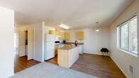 Located at 550 Larkspur Street in Ponderay, Idaho, Unit D309 is a thoughtfully laid-out single-floor residence that combines practicality with comfortable living. The open-concept kitchen is a standout feature, showcasing light maple cabinetry, laminate countertops, a center island with additional prep space, and a full suite of white appliances including a refrigerator, electric range, and dishwasher. Wood-look flooring runs throughout the kitchen, adding warmth and easy maintenance. The spacious living area is carpeted and bathed in natural light, courtesy of large sliding glass doors that open directly onto a private balcony with a railed surround and tree-lined views. The bedroom is generously sized with plush carpet, a natural light-filled window with outdoor views, and a dedicated closet offering ample storage. The bathroom is clean and functional, featuring a full soaking tub and shower combination, wood-look flooring, and a vanity with matching cabinetry. Neutral tones throughout the residence create a bright, cohesive atmosphere. The overall layout is efficient and well-connected, making this unit a practical and inviting space in the heart of Ponderay.