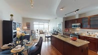 This generously sized one-bedroom, one-bathroom residence offers a well-designed open-concept layout across a single floor. The kitchen is a standout feature, appointed with rich dark-wood cabinetry, granite countertops, a large center island with a built-in sink, stainless steel appliances including a gas range and French door refrigerator, a wine cooler, and hardwood flooring. Track lighting illuminates the space, which flows seamlessly into the dining area and living room.

The living room is bright and airy, benefiting from floor-to-ceiling windows and direct access to a private balcony offering sweeping panoramic views. A flexible secondary room with hardwood floors and a ceiling fan functions effectively as a home office or den.

The bedroom is carpeted and spacious, featuring a ceiling fan and a direct en suite connection to the bathroom. The bathroom is elegantly finished with large-format tile, a glass-enclosed walk-in shower with a pebble-stone floor, and a soaking tub, creating a spa-like atmosphere. Throughout the residence, neutral tones and quality finishes contribute to a refined, comfortable ambiance.