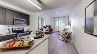 Located at 350 E Congress St in the heart of downtown Tucson, Arizona, this one-bedroom, one-bathroom unit offers a well-designed, efficient layout with modern finishes throughout. Light-toned hardwood-style flooring flows across the entire floor plan, unifying the open-concept living and kitchen areas. The kitchen is outfitted with dark espresso cabinetry, granite countertops, a tile backsplash, and a full suite of stainless steel appliances including a refrigerator, electric range, and microwave. A peninsula counter provides additional prep space and separates the kitchen from the living area. The living room is bright and inviting, benefiting from natural light through large windows dressed with curtains and blinds, with an exposed concrete structural column adding an industrial design accent. The bedroom features a sliding barn-style door, a dedicated closet, and a window with outdoor views. The bathroom includes large-format tile flooring, a soaking tub with white subway tile surround, and a vanity with dark cabinetry. A dedicated laundry area and a hallway complete the thoughtfully organized floor plan.