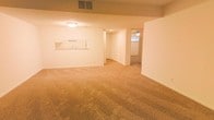 This single-floor residential space offers an open and functional layout designed for comfortable everyday living. The main living area is expansive, featuring wall-to-wall carpeting in a warm neutral tone that adds softness underfoot and a cohesive feel throughout the space. The ceiling is finished with a textured surface and equipped with a flush-mount light fixture, providing consistent ambient lighting.

A standout feature is the pass-through kitchen window, which connects the kitchen to the main living area, promoting an open and communicative flow between spaces. The kitchen area is visible through this cutout, hinting at a practical and efficiently arranged cooking space with counter access.

From the living area, a hallway leads to additional rooms, one of which is visible with its own ceiling fan, suggesting it functions as a bedroom or secondary living space. The corridor provides a clear sense of depth and connectivity throughout the unit.

The interior palette is clean and neutral, with white walls throughout that enhance the sense of brightness and openness. Ventilation is provided via ceiling-mounted HVAC vents, ensuring year-round climate comfort. Overall, the space presents a straightforward, well-maintained layout suited for a variety of living arrangements.