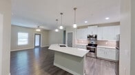 This single-floor unit showcases a thoughtfully designed open-concept layout with a seamless flow between the kitchen, dining, and living areas. The kitchen serves as the focal point, featuring crisp white shaker cabinetry extending to the ceiling, white quartz countertops, and a full suite of stainless steel appliances including a refrigerator, electric range, and over-the-range microwave. A generously sized central island with an undermount sink and pendant lighting overhead adds both functionality and visual appeal. Neutral-toned subway tile backsplash and under-cabinet lighting complement the kitchen's modern aesthetic.

Dark hardwood-style flooring runs throughout the main living areas, providing a striking contrast against the light gray walls and white trim. The open living space is illuminated by recessed lighting and a ceiling fan, while a window allows natural light to filter in.

The bedrooms feature the same hardwood-style flooring, ceiling fans, and windows for natural light. The bathrooms are well-appointed, with white vanities, quartz countertops, brushed nickel fixtures, framed mirrors, and tiled shower surrounds. Stylish gray interior doors with panel detailing add a refined touch throughout the unit.
