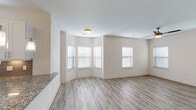 This well-designed single-story unit presents a clean, modern aesthetic throughout its open-concept floor plan. The living and dining areas are finished with light wood-tone luxury vinyl plank flooring and neutral painted walls, creating a bright and airy atmosphere. Multiple windows dressed with white blinds allow natural light to flow generously through the space, while ceiling fans are installed in the main living areas and bedrooms for added comfort.

The kitchen is a standout feature, outfitted with crisp white shaker-style cabinetry, granite countertops, a taupe subway tile backsplash, and a full suite of stainless steel appliances including a refrigerator, electric range, and over-the-range microwave. A peninsula with a granite overhang opens toward the living area, reinforcing the open-concept design. A door from the kitchen provides direct exterior access.

The bedrooms are carpeted in neutral tones and each include ceiling fans and window access to natural light. One bedroom includes access to a walk-in closet. The bathroom is finished with white cabinetry, granite countertops, wood-look vinyl flooring, and a glass-enclosed walk-in shower with marble-style tile surround.
