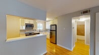 This single-floor residence offers a cohesive, modern design throughout, unified by warm hardwood flooring that extends across the main living areas and bedrooms. The open-concept living and dining area is bright and airy, featuring a ceiling fan with light fixture and access to an exterior door with sidelights that invite natural light into the space.

The kitchen is thoughtfully designed with a peninsula-style breakfast bar that connects it to the living area, providing both a functional workspace and a casual dining option. White cabinetry with sleek bar-pull hardware lines the walls, complemented by stainless steel appliances including a range, microwave, dishwasher, and refrigerator. A stainless steel sink is positioned beneath a window overlooking the outdoors, and a pendant light adds a finishing touch.

The bedrooms offer comfortable layouts, with one room featuring dual closets and another with a wide window framing outdoor greenery and a single closet. The bathroom is finished with large-format earth-toned ceramic tiles surrounding a full soaking tub and shower combination, with brushed nickel fixtures completing the look. The overall palette of soft gray walls and white trim gives the space a clean, neutral aesthetic throughout.