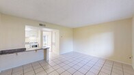 Located at 744 Spring West Rd in Orlando, FL, this one-bedroom, one-bathroom unit offers a well-organized layout across a single floor. The combined living and dining area is bright and open, featuring large light-colored ceramic tile flooring, soft cream-toned walls, and natural light streaming in through a wide window with views of the surrounding greenery. The kitchen is positioned adjacent to the living area, separated by a breakfast bar with a dark granite countertop. White cabinetry, a gas range, and a built-in microwave complete the functional cooking space. A dedicated entry area provides a welcoming transition into the home. The bedroom is carpeted for comfort and features a sliding glass door that opens to an outdoor balcony with exterior views, as well as access to a dedicated walk-in closet equipped with shelving and hanging rods. The bathroom includes white cabinetry with brushed nickel hardware, a granite-topped vanity, a wall-mounted towel bar, and a shower-tub combination, all finished with consistent tile flooring that carries throughout the wet areas. The overall ambiance of the unit is clean, neutral, and functional, making it a practical and comfortable living space in the Orlando area.
