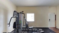 Located at 190 N Corry Field in Pensacola, Florida, this single-floor fitness facility provides a functional and focused workout environment. The exercise space features neutral-toned walls that create a clean, distraction-free atmosphere conducive to training. Dark rubber flooring covers the workout area, offering durability and safety underfoot — a practical choice for a high-use fitness setting. The room is equipped with a multi-station strength training machine, allowing users to perform a variety of resistance exercises in one location. A window fitted with horizontal blinds allows natural light to filter into the space, brightening the interior while maintaining privacy. The textured ceiling adds a classic architectural finish to the room. The layout is straightforward and efficient, maximizing the usable floor space for equipment and movement. Overall, this facility presents a no-frills, purpose-built environment designed to meet the essential fitness needs of its users, making it a practical resource for those seeking a convenient and accessible place to exercise in the Pensacola area.