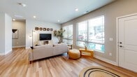 This single-story residence is designed with a cohesive, modern aesthetic defined by warm neutral tones, wood-look flooring, and recessed lighting carried consistently throughout. The open-concept kitchen is a functional centerpiece, featuring dark espresso cabinetry, granite countertops, a large island with bar seating, stainless steel appliances, and pendant lighting — all flowing seamlessly into a dedicated dining area and a spacious living room. The living area benefits from an abundance of natural light provided by multiple large windows fitted with blinds, offering views of the surrounding exterior. The bedroom is a comfortable retreat, showcasing a generous window that further enhances natural light, and direct access to a roomy walk-in closet outfitted with wire shelving and wood-look flooring for practical storage. The full bathroom includes a dark-toned vanity with granite countertop, a wide mirror, and a tub-shower combination. The overall ambiance of the residence is bright, clean, and contemporary, with design choices that balance style and practicality throughout each area of the space.