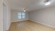 This single-story residence offers a well-organized layout with a neutral color palette of warm beige and white tones throughout. Light wood-style flooring runs through the main living areas, complemented by textured ceilings and clean white baseboards that provide a crisp, finished look.

The open living area connects to a kitchen featuring white cabinetry, light countertops, a white subway tile backsplash, and a full suite of stainless steel appliances, including a refrigerator, electric range, microwave, and dishwasher. A stacked washer and dryer unit is conveniently integrated into the kitchen area. A pass-through counter separates the kitchen from the living space, enhancing the open feel. Natural light enters through blinded windows, and a ceiling fan with a light kit provides both comfort and illumination.

The bedrooms are carpeted in a neutral tan tone, each featuring large windows with exterior views and ceiling fans. The bathroom is finished in white, offering a vanity with a mirrored medicine cabinet, a toilet, and a shower/tub enclosure with matching wood-style flooring. The overall ambiance is clean, functional, and move-in ready.